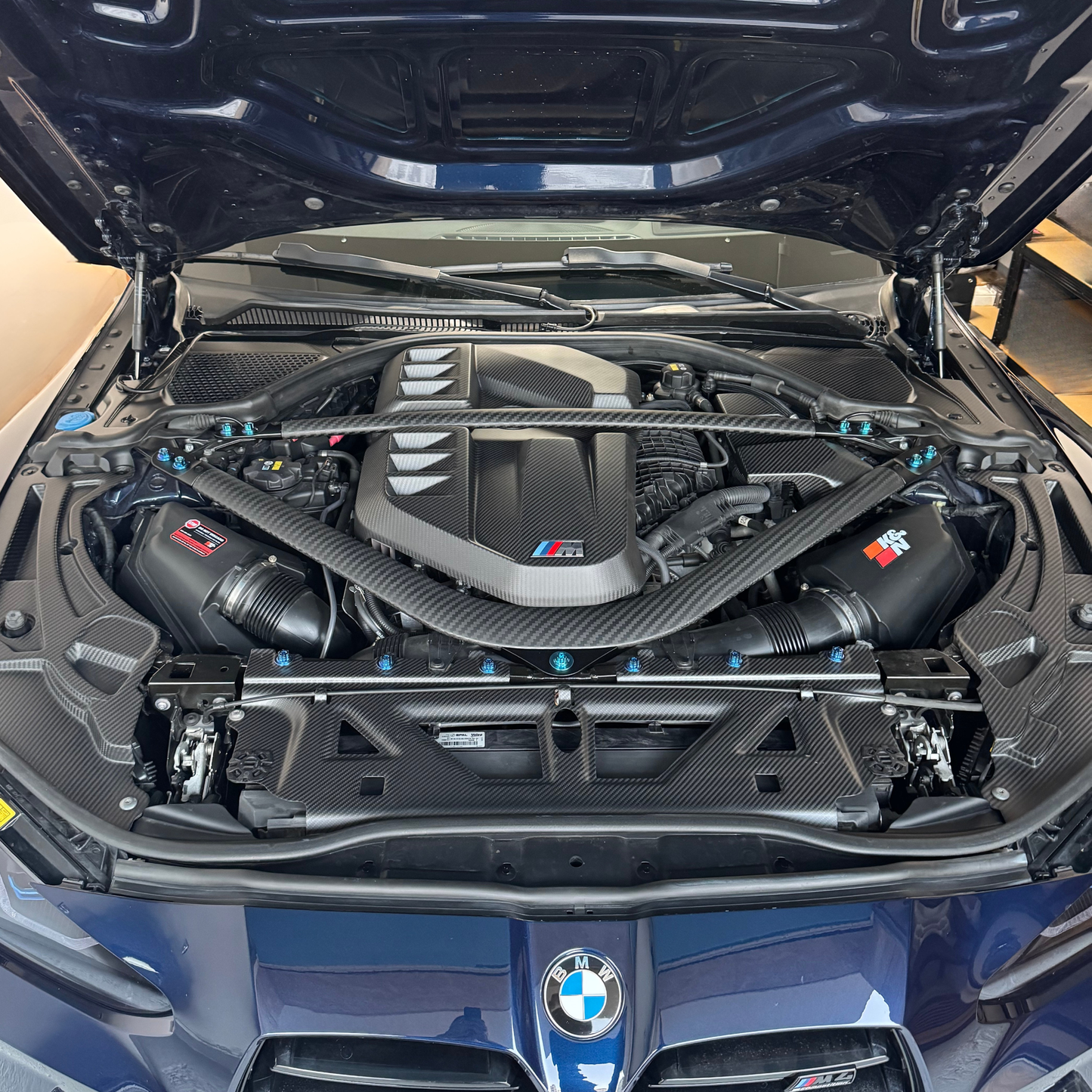 Open hood of a BMW car revealing the engine with visible branding.