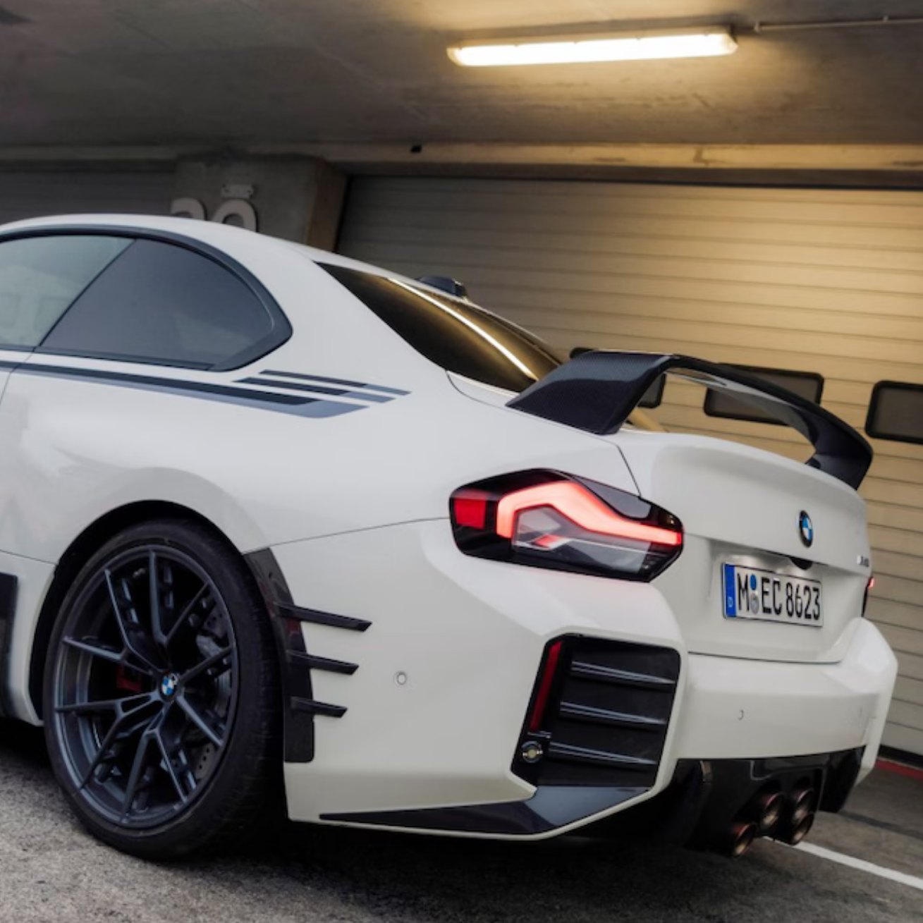 White sports car with black rims and a spoiler in a garage.